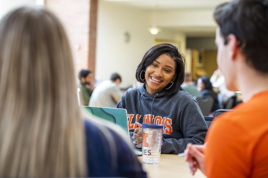 Two female students share a laptop and work on a project in the Business Instructional Facility commons area.